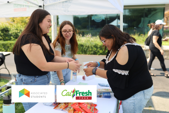 Two student staff handing a CalFresh flier to a student at a pop-up table.