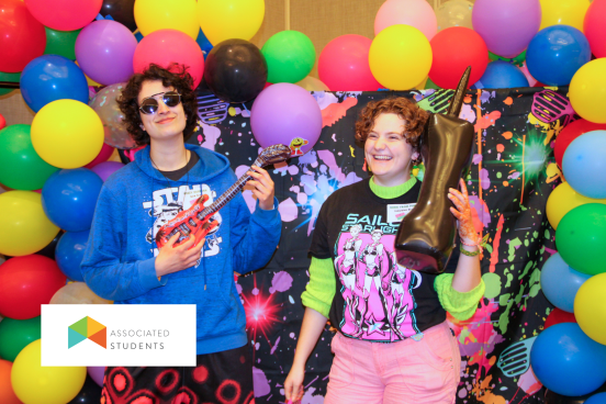 Students dressed in 80's clothes posing in front of a retro balloon backdrop.