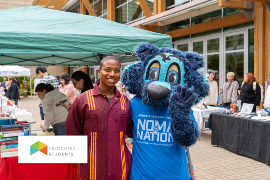 Student posing with Lobo in front of a vendor stand in Seawolf Plaza.