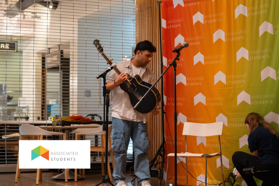Student holding guitar in W&B in front of an AS Logo backdrop. 