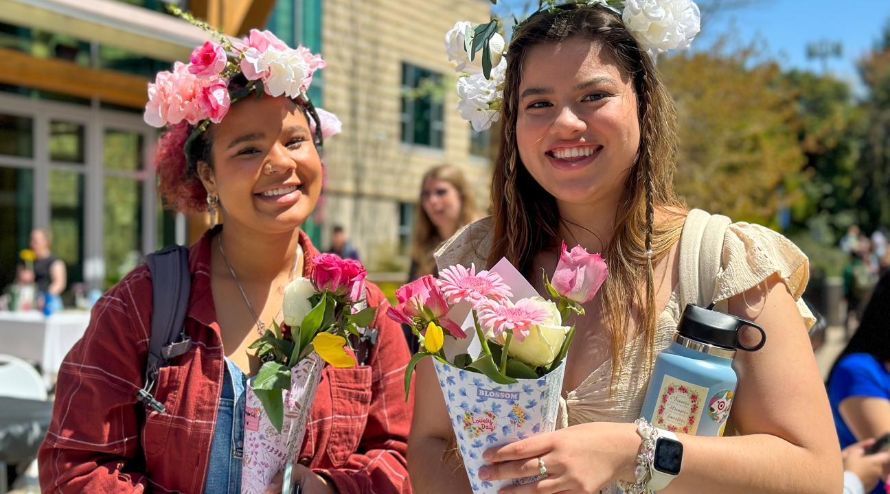Two students wearing flower crowns and holding flowers.