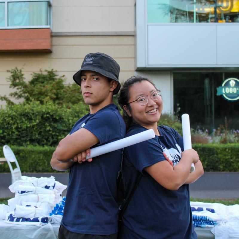 Two students posing back to back holding glow sticks.