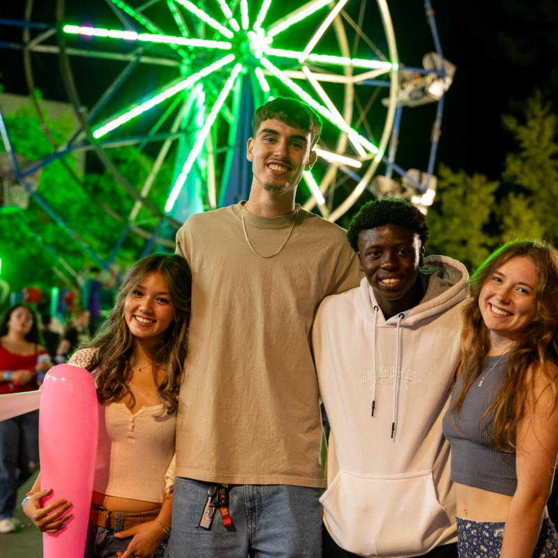 Four students posing with a ferris wheel in the background.