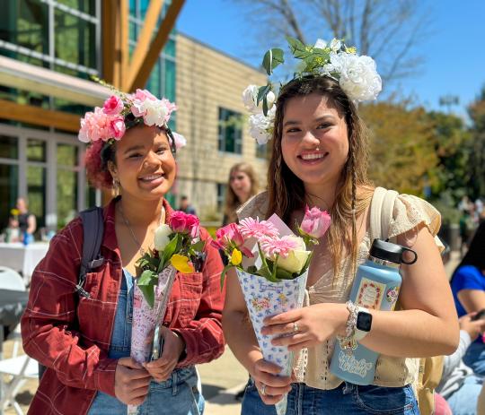 Two students wearing flower crowns and holding flowers.