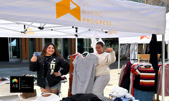 Two students holding up clothes at a JUMP Pop Up tent.