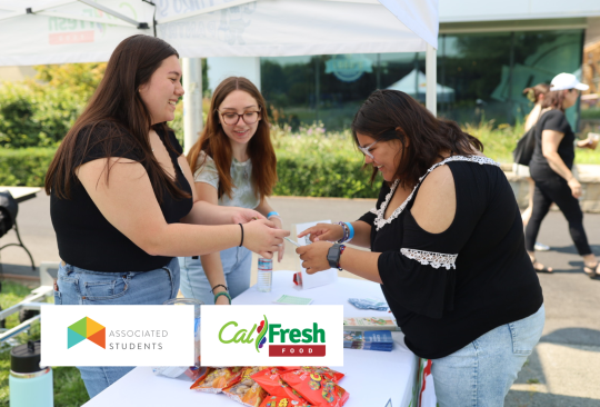 Two student staff handing a CalFresh flier to a student at a pop-up table.