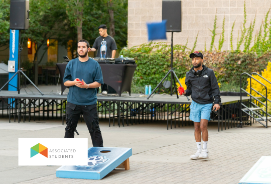 Students playing cornhole in Seawolf Plaza with a DJ in the background.
