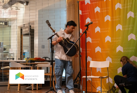 Student holding guitar in W&B in front of an AS Logo backdrop. 