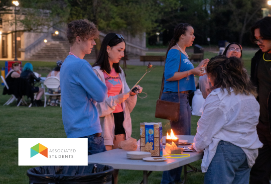 Three people roasting marshmallows over a small tabletop fire pit.