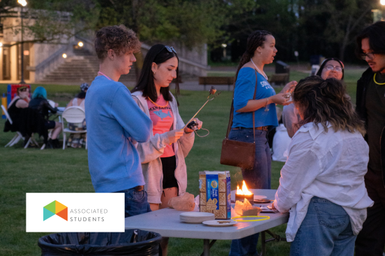 Three people roasting marshmallows over a small tabletop fire pit.